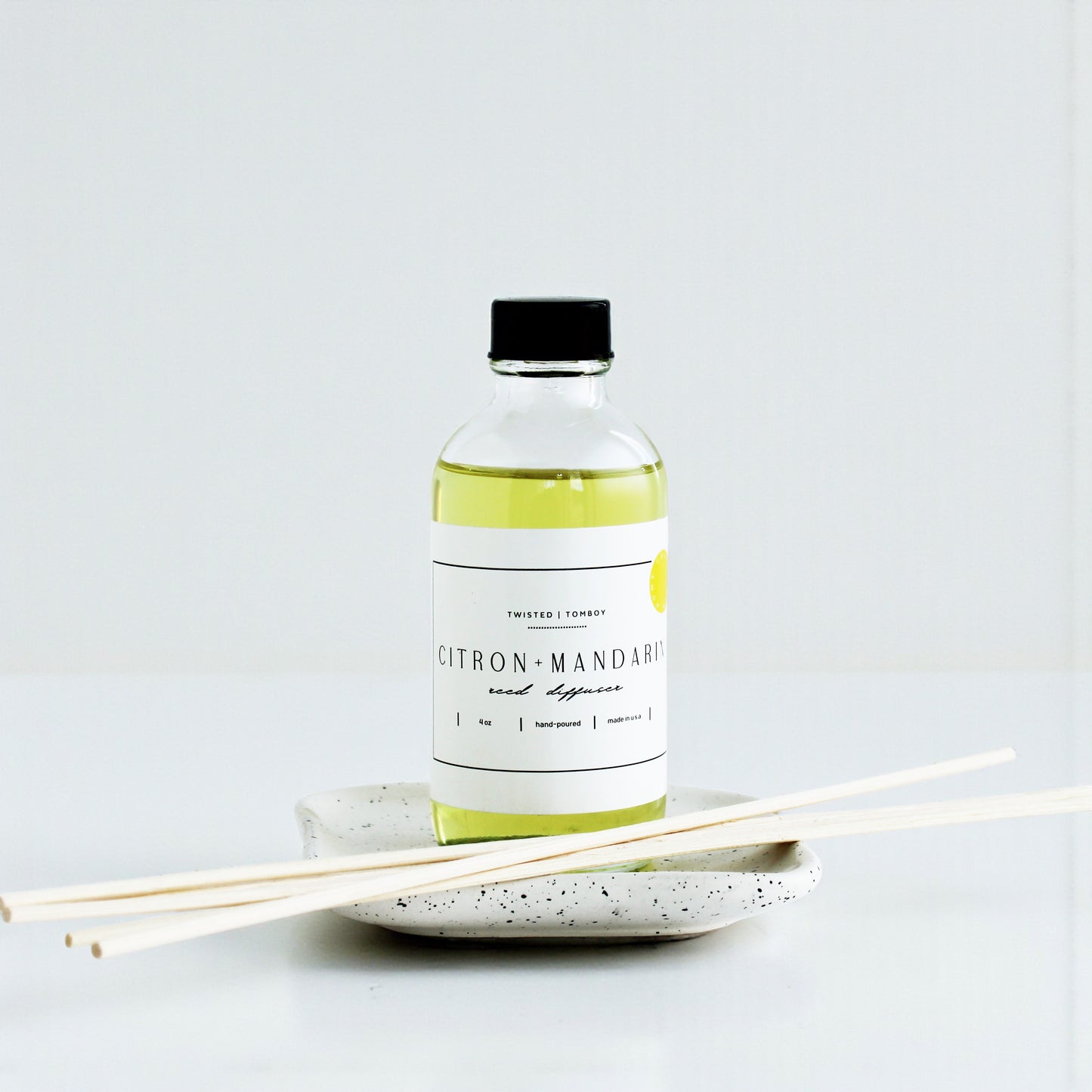 Reed diffusers in six scents, featuring a green citron-mandarin bottle and natural reed sticks on a speckled dish.