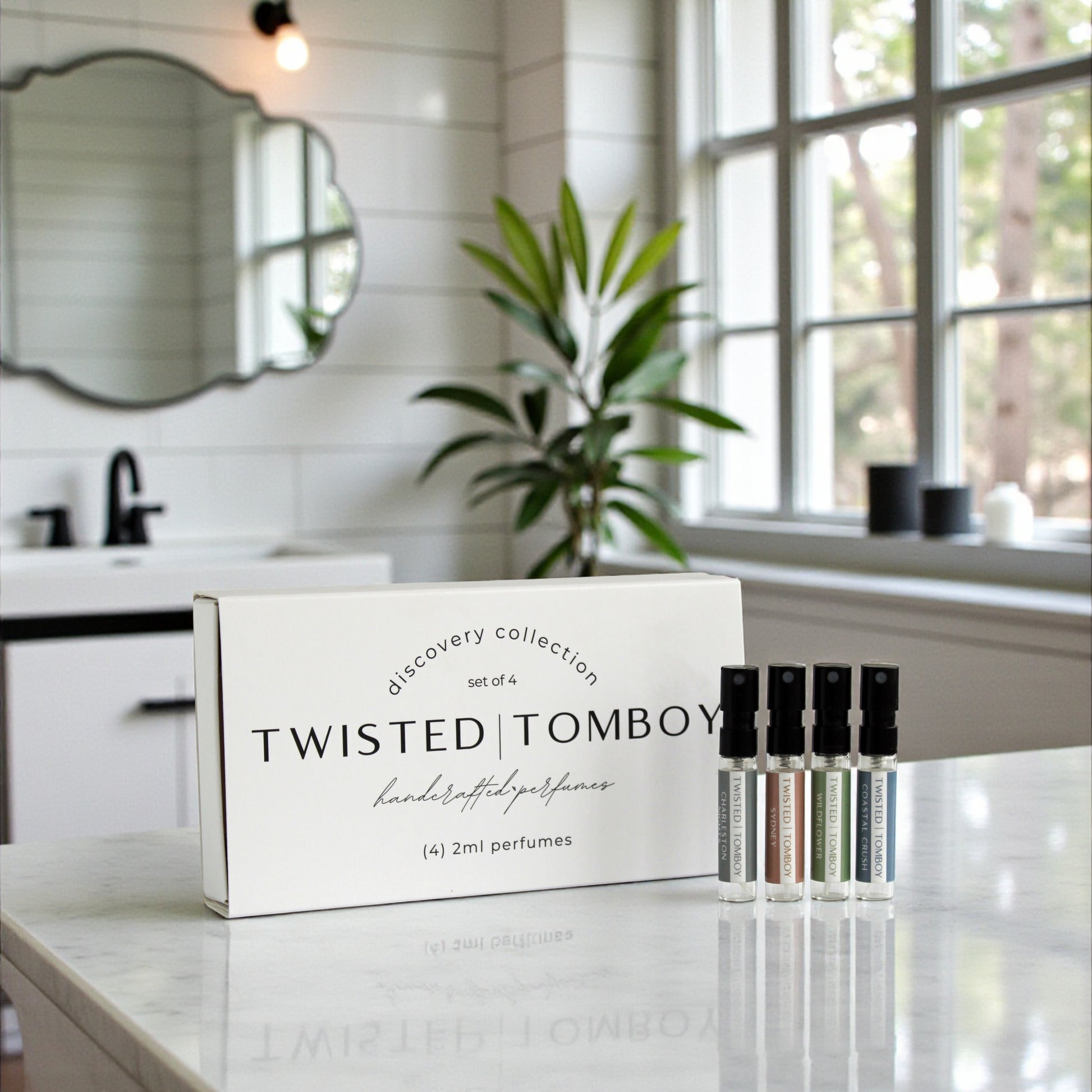 Twisted Tomboy perfume set on a bathroom counter with a window and plant in the background