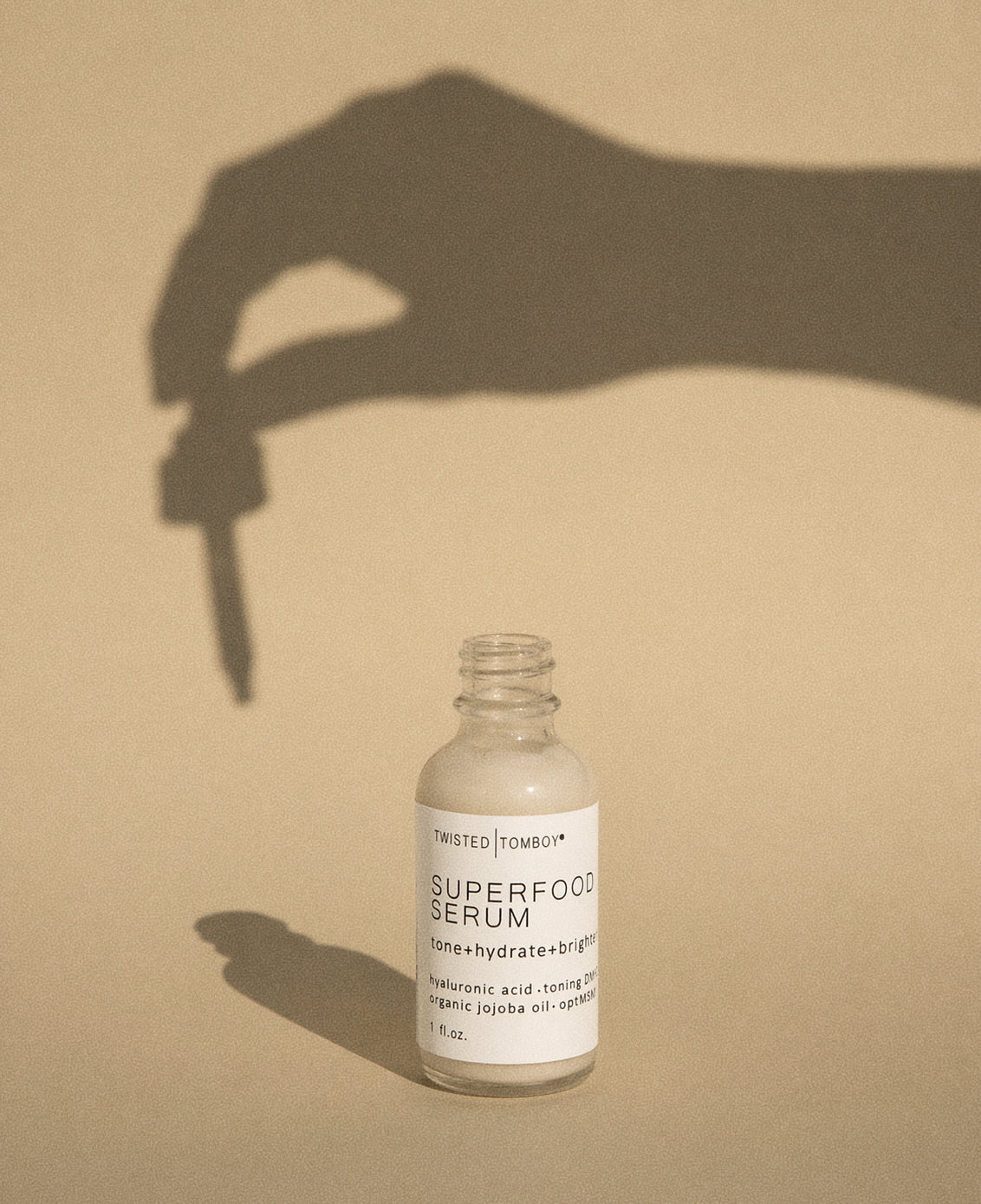 Superfood serum bottle with a hand holding a dropper shadow on a beige background