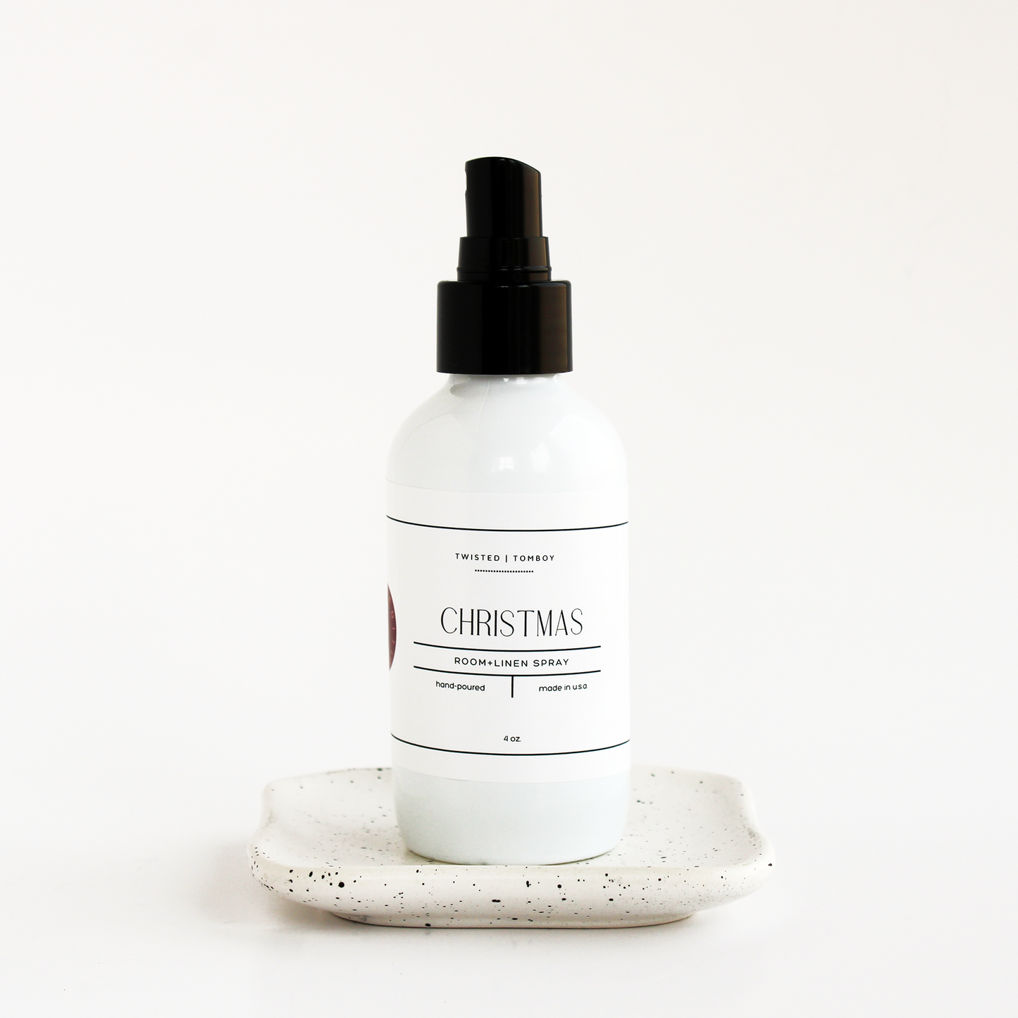 White spray bottle labeled 'Christmas' on a speckled ceramic plate with a white background